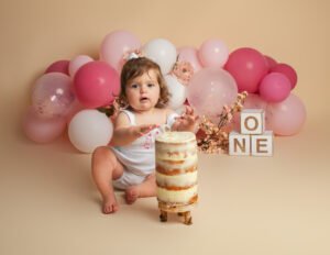 1 year old girl putting her hands into a cake during her cake smash photo shoot