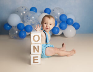 baby boy cat on a blue backdrop with a cream floor touching blocks spelling one the number one
