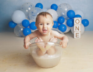 baby boy sat in a clear plastic bath prop on a blue backdrop with blue and white balloons