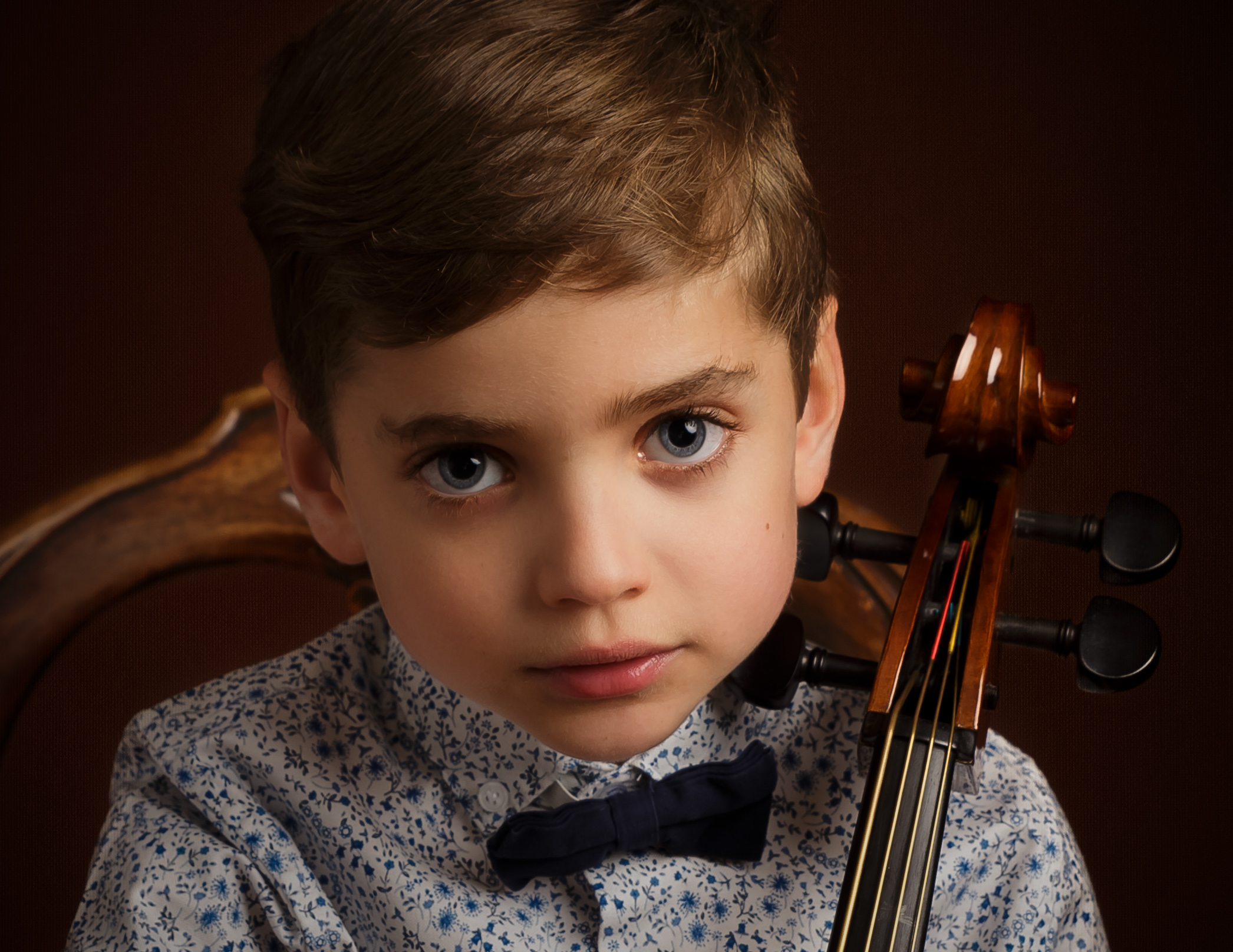 Boy with big blue eyes sat with his Cello by family photographer in basingstoke hampshire