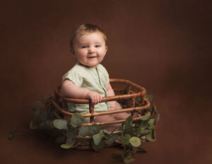 6 month milestone photo shoot. baby boy sitting unaided in bamboo basket wearing a green top