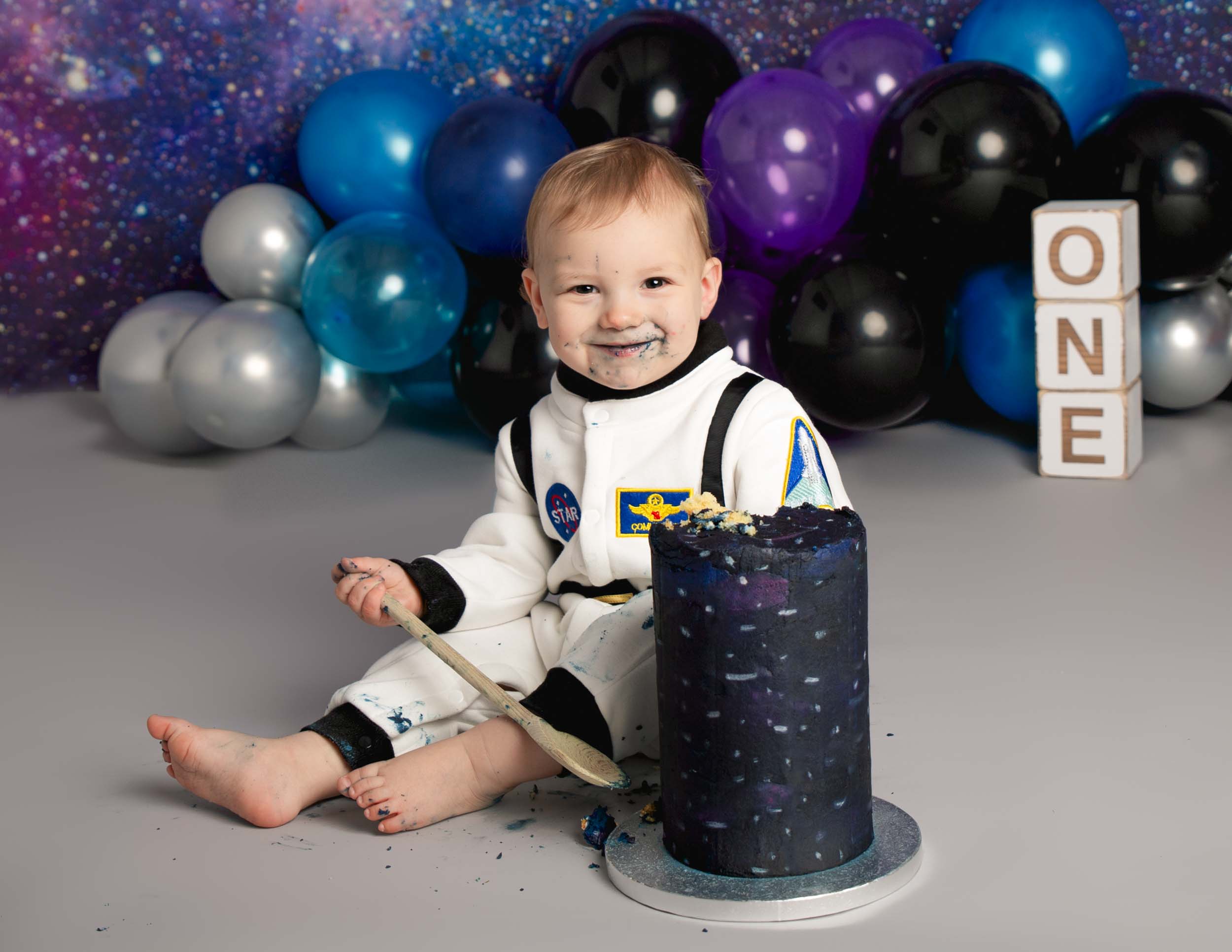 1 year old boy sat in astronaut onesie eating cake