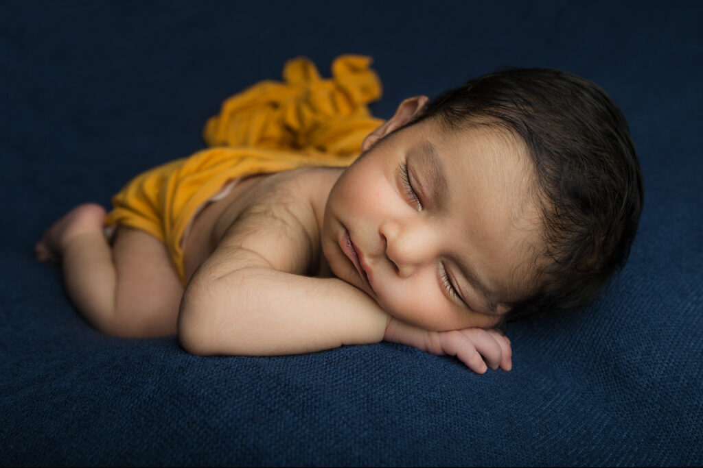 baby on a blue back ground in chin on hands pose.  My top 5 Newborn Poses